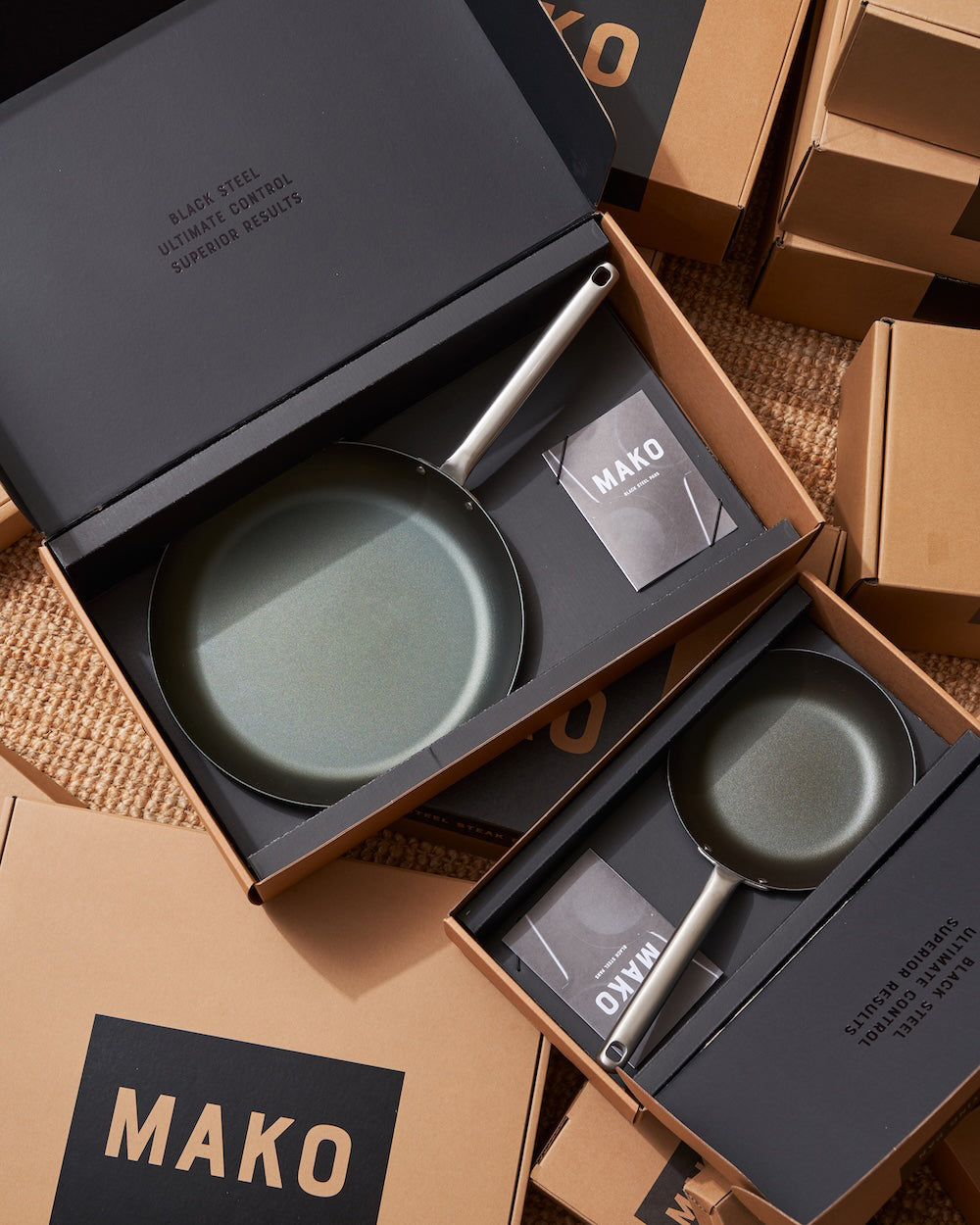 Nonstick MAKO frying pans in gift boxes on a textured surface, premium cookware set display