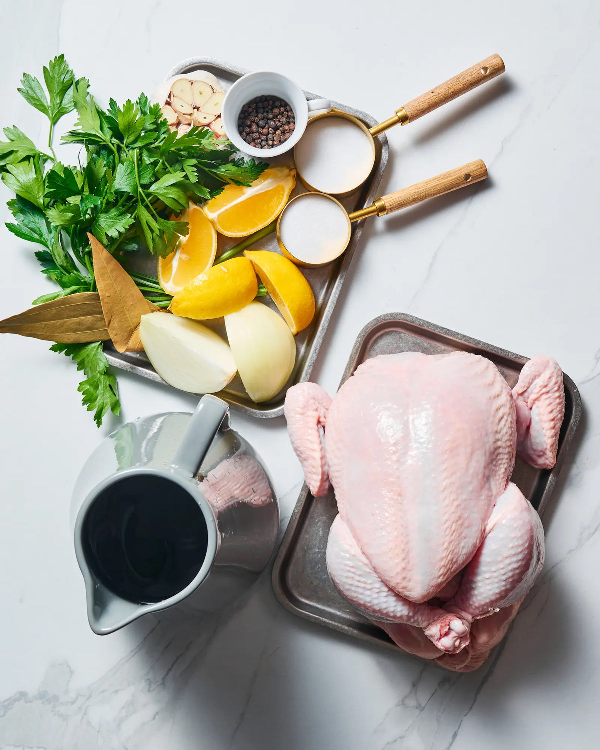 Raw whole chicken with lemon wedges, garlic, onion, fresh herbs, bay leaves, peppercorns, salt, sugar and water arranged for making a wet brine.