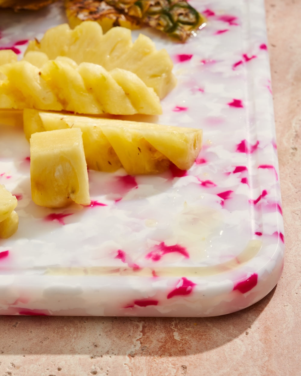 Sliced pineapple on a white and pink marbled resin cutting board on a stone counter