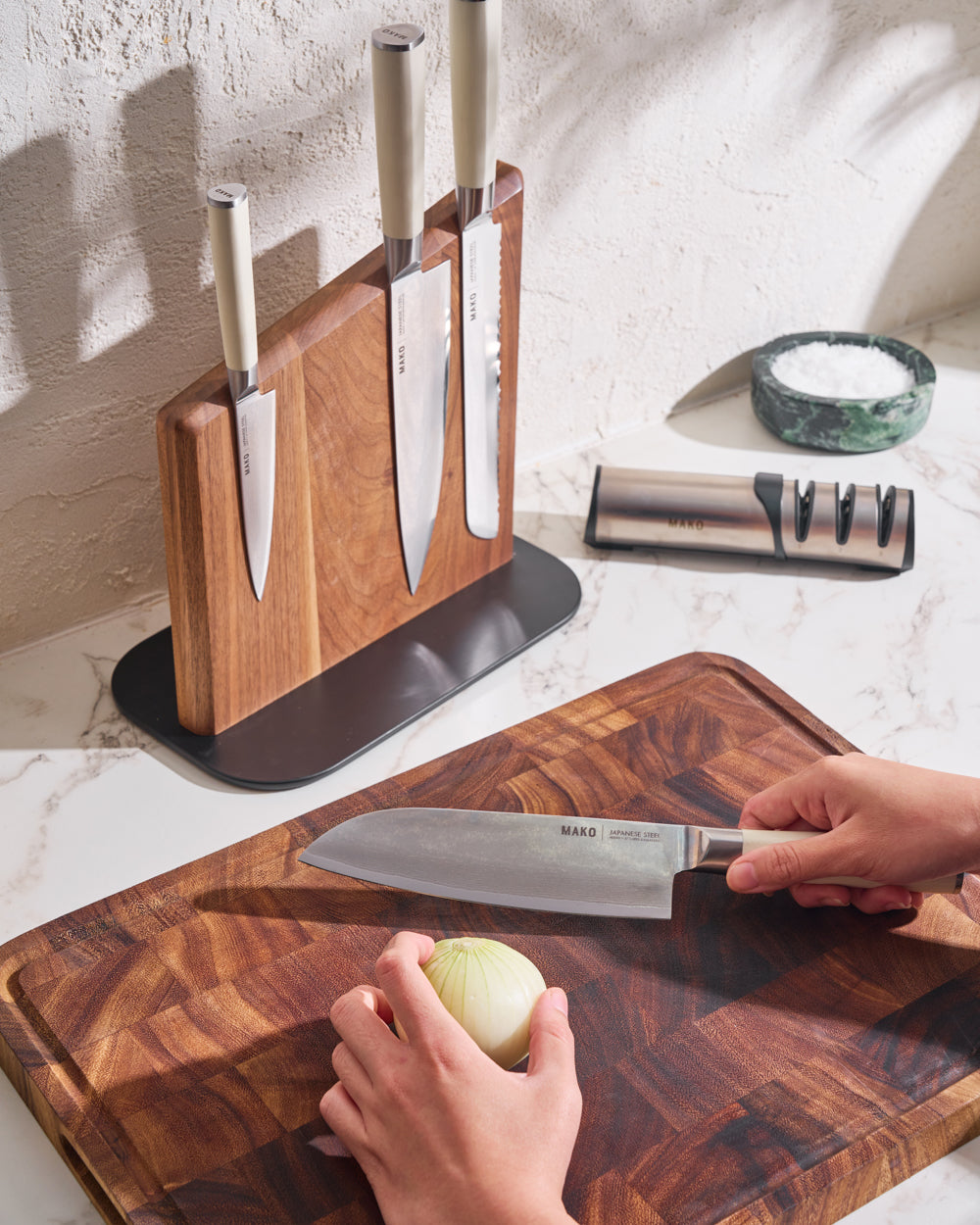MAKO Japanese Steel Knife Set of 4 - Cream Magnetic Stand hand with white santoku knife about to chop peeled onion