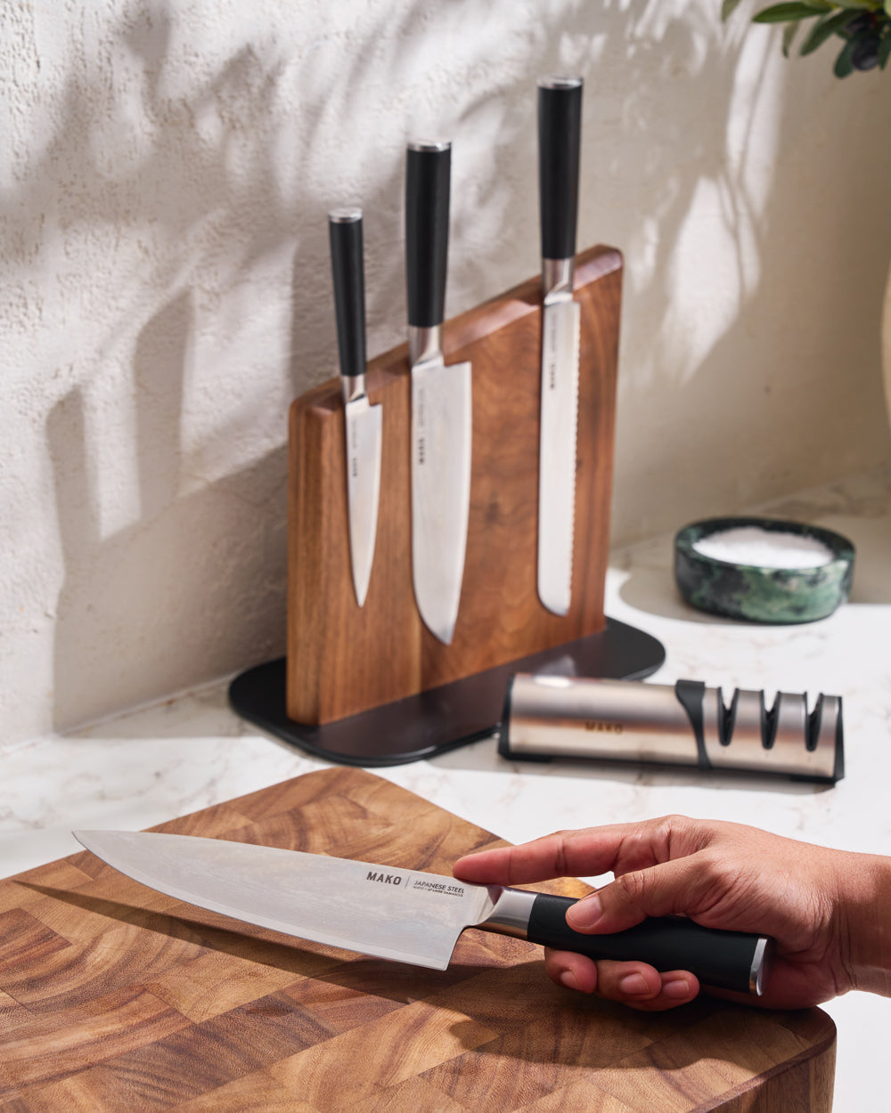 MAKO Japanese Steel Knife Set of 4 - Black Magnetic Stand Chef knife in hand with remaining set in background.