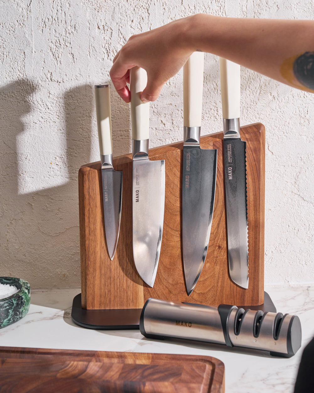 MAKO Japanese Steel Knife Set of 4 - Cream Magnetic Stand hand lifting White Santoku knife off block with sharpener in front and chopping board
