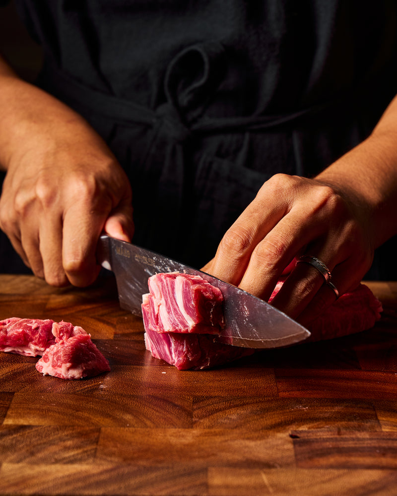 A close-up of a person's hands slicing raw red meat with a MAKO chef knife