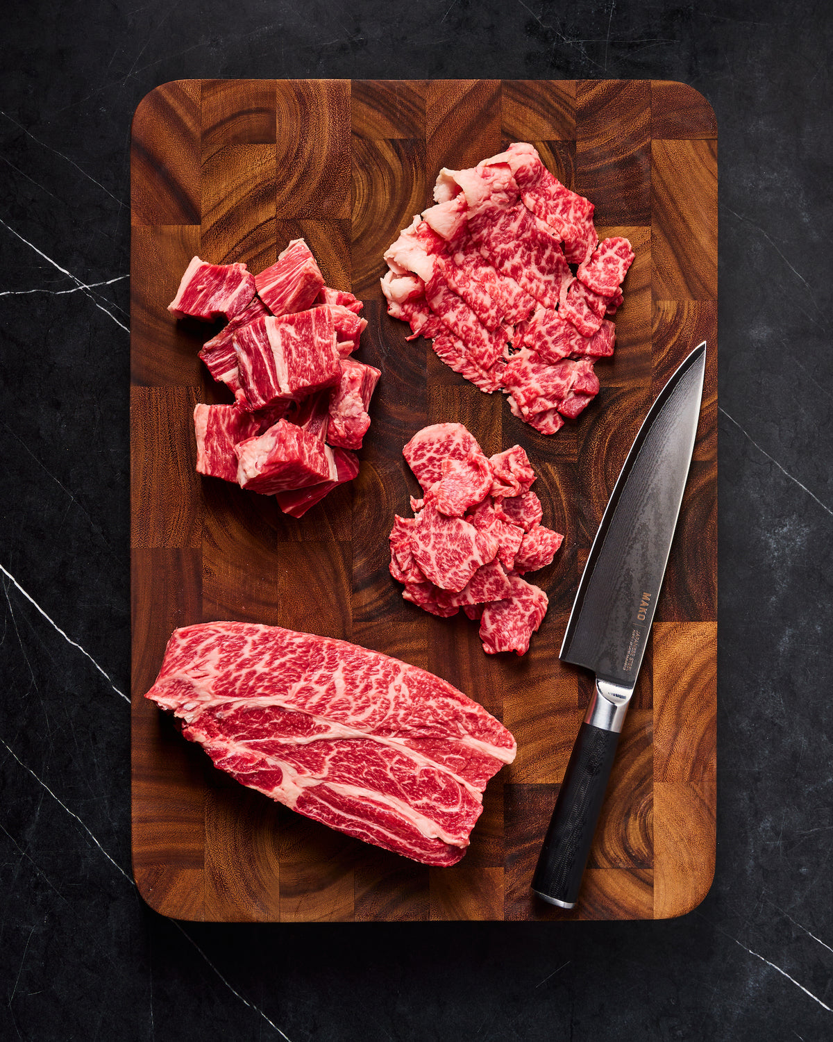 Raw beef cuts arranged on a wooden cutting board next to MAKO chef knife 
