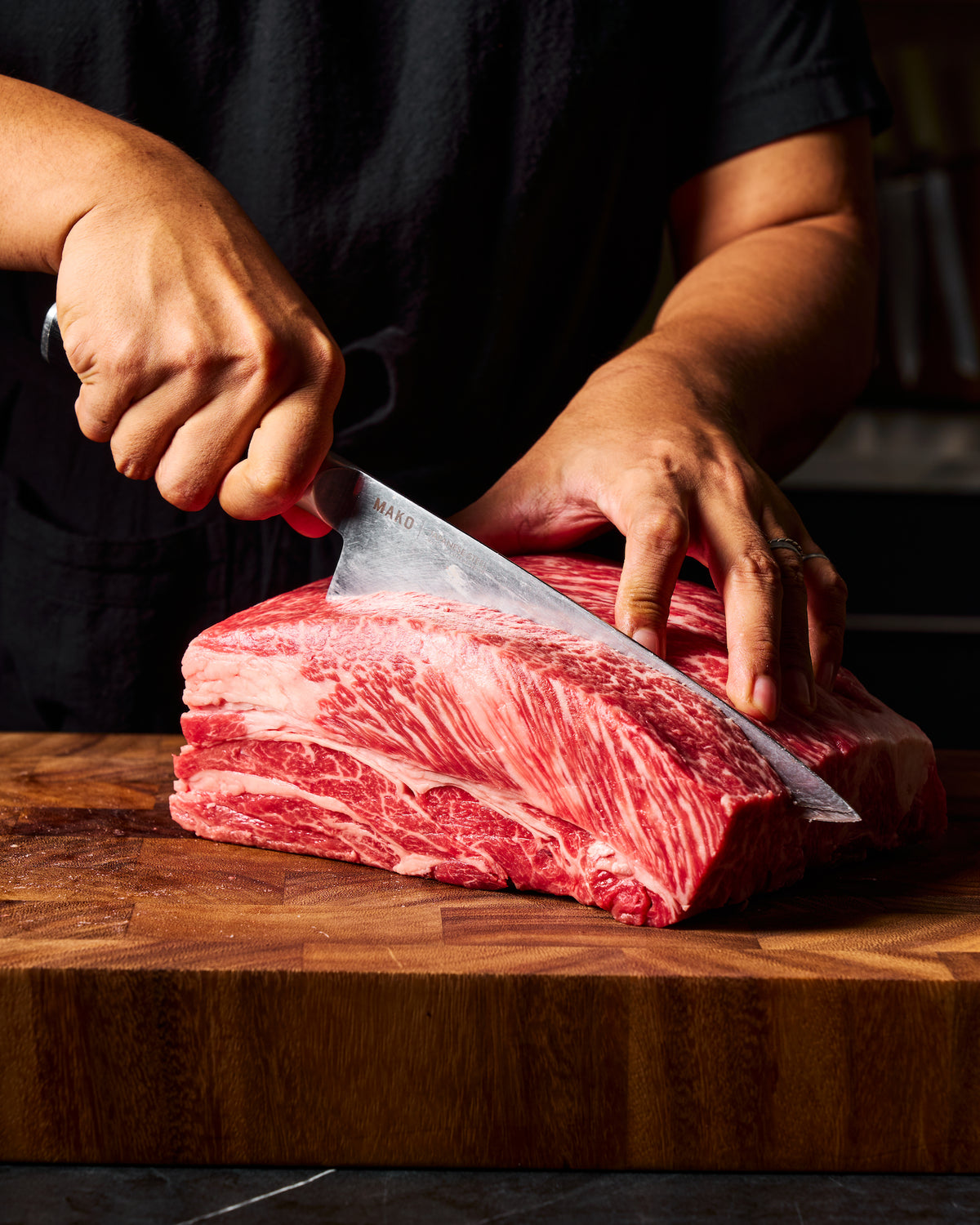 A close-up of a person's hands slicing raw meat with a MAKO chef knife