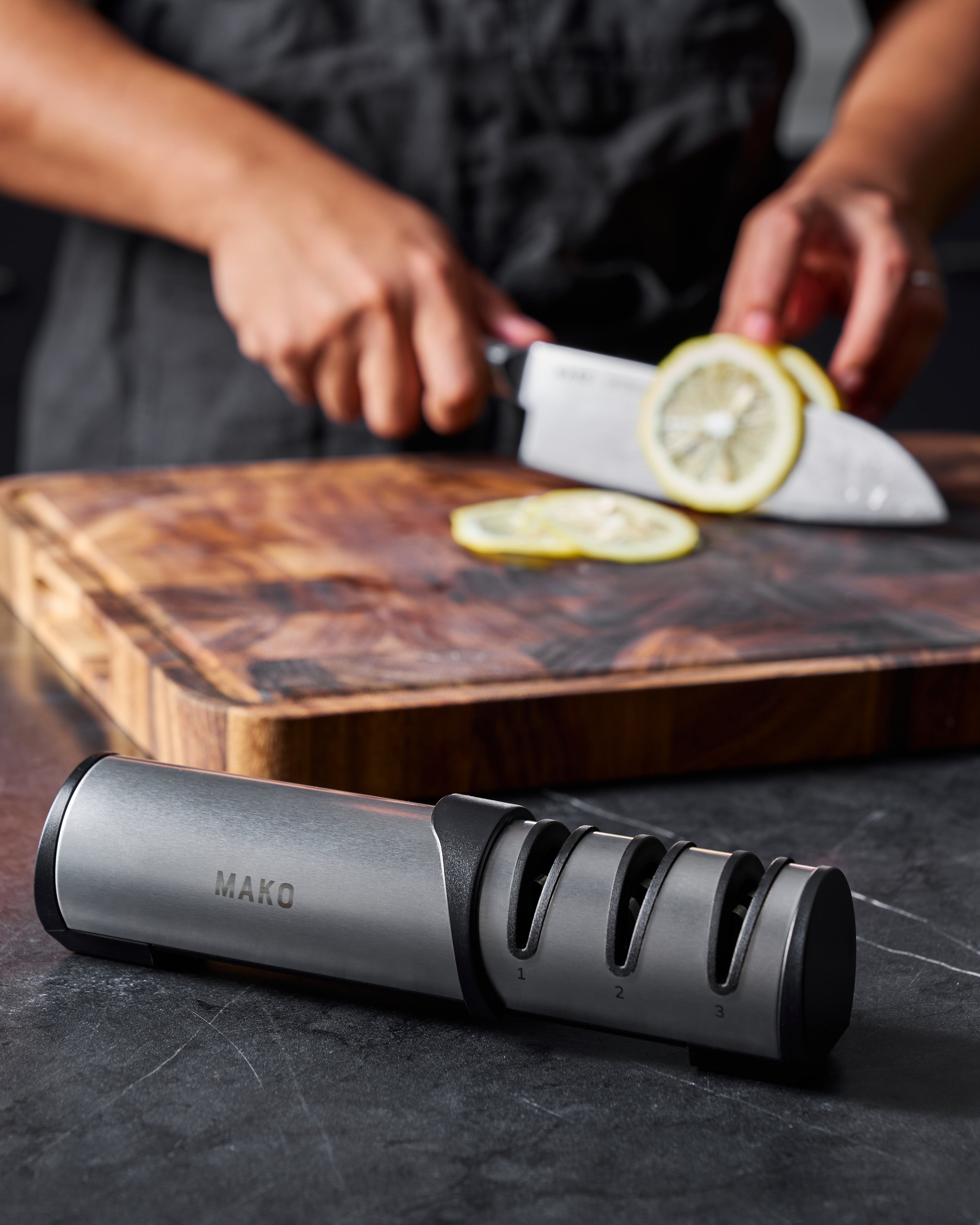 Hand using kitchen knife to slice lemon on a wooden cutting board with a MAKO knife sharpener