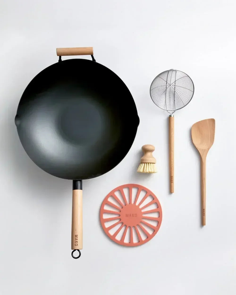 Black nonstick wok with wooden handle, cooking utensils, scrub brush, and orange trivet on white background