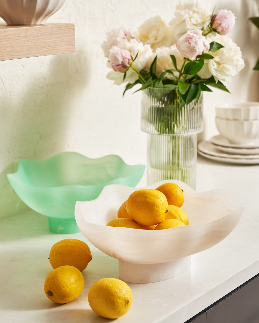 Modern countertop with sculptural bowls filled with lemons and a glass vase of pink and white flowers