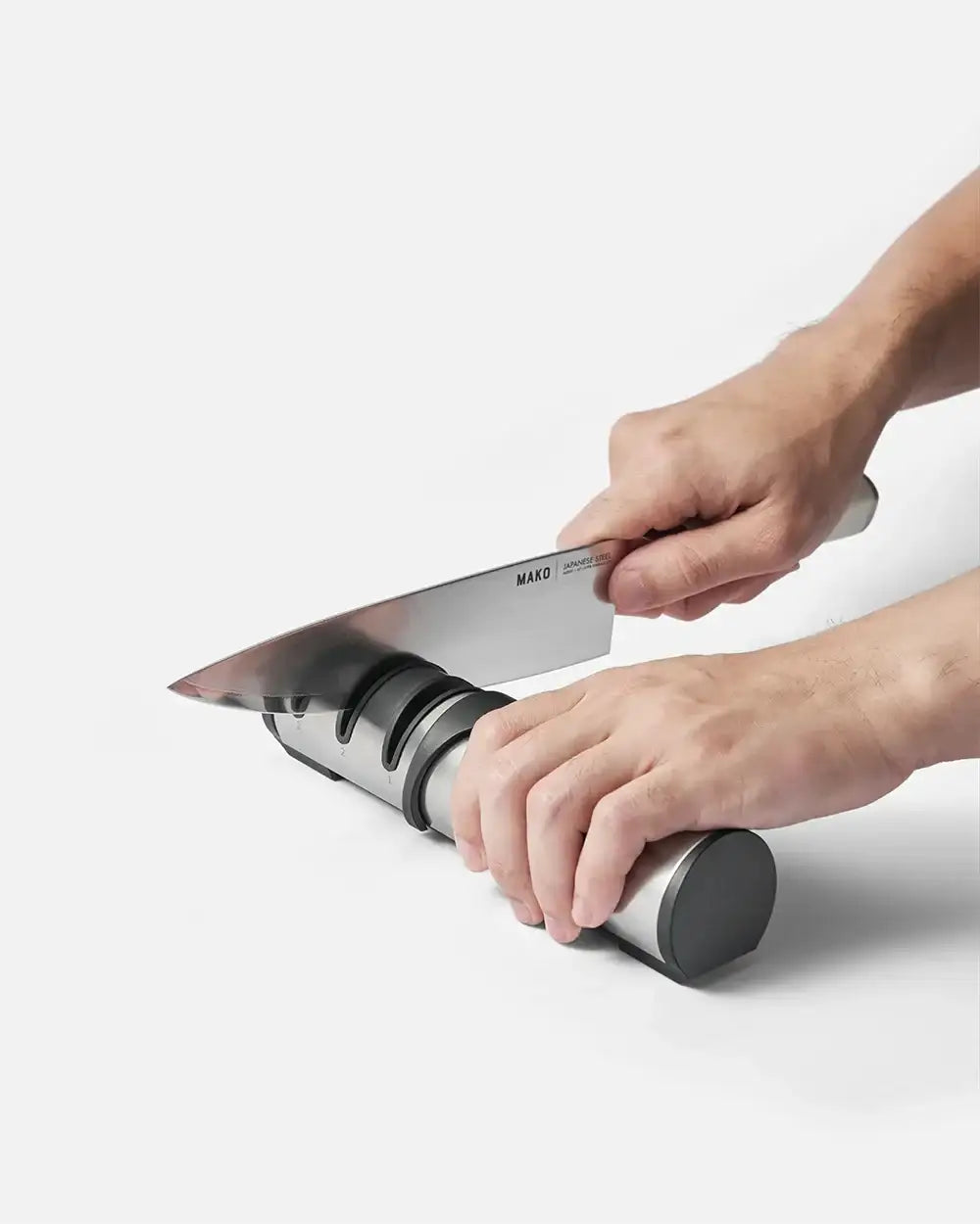 Hands sharpening a Mako Japanese steel knife on a stainless steel knife sharpener