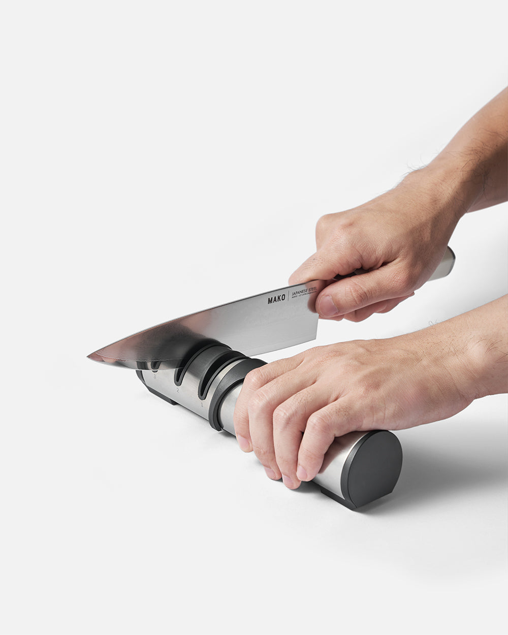 Hands sharpening a kitchen knife on a two-stage knife sharpener on a white surface
