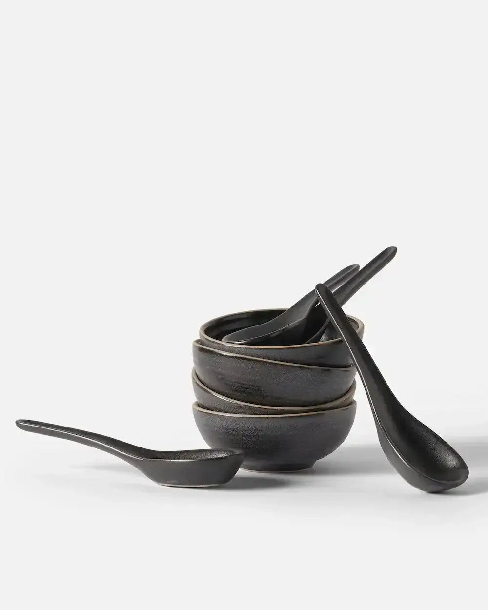 Stack of three black ceramic bowls with matching spoons on white background Asoke by Marion Grasby