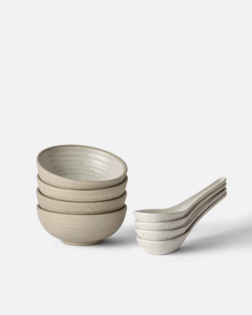 Stacked ceramic mini bowls and matching spoons in neutral tones on white background