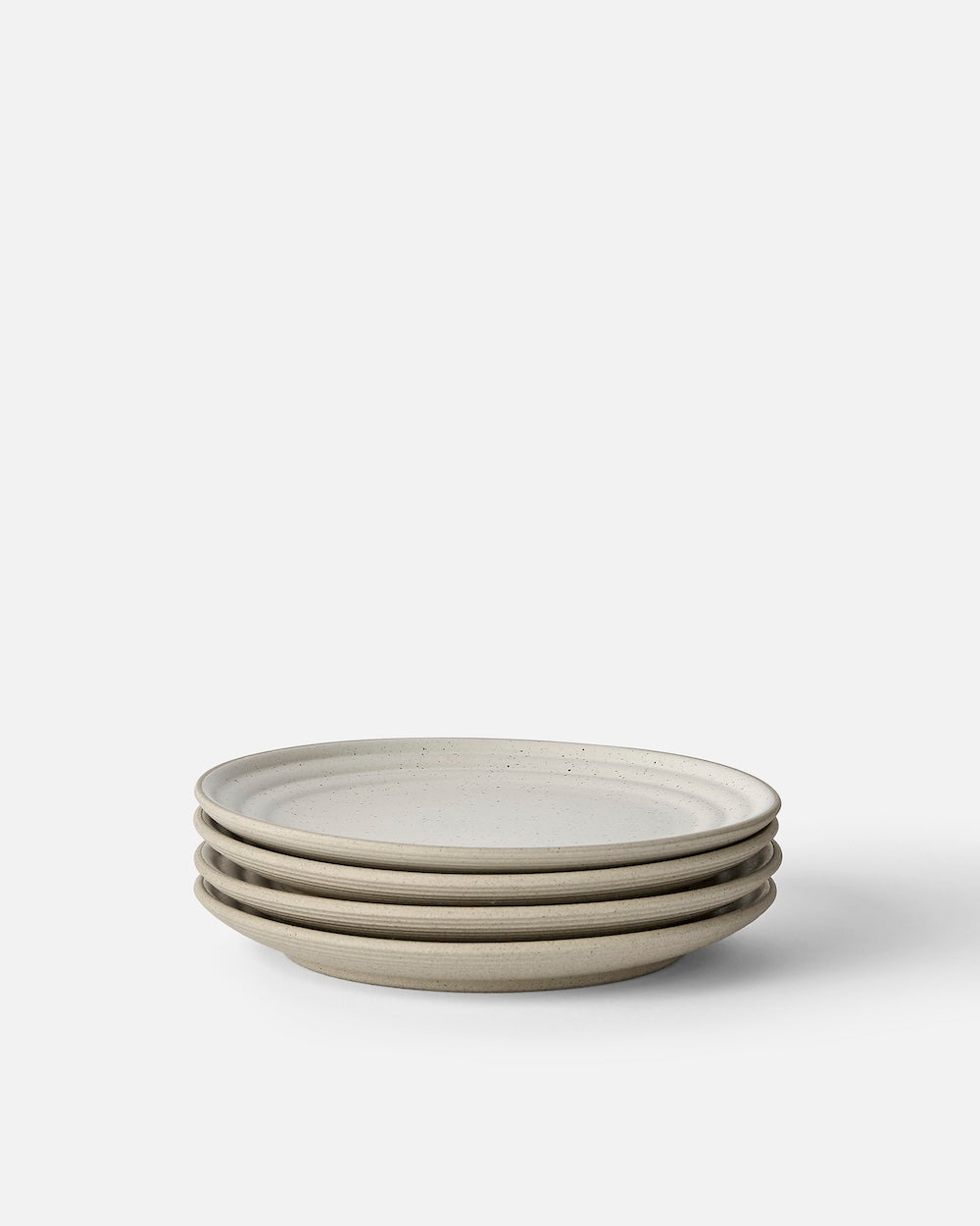 Stack of four beige stoneware side plates with subtle speckle on white background