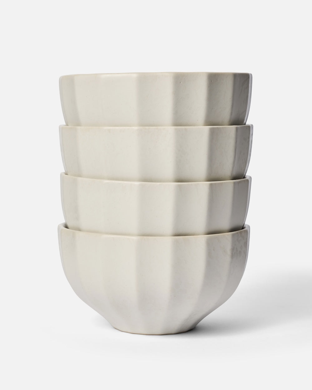Set of four white ceramic noodle bowls with fluted sides stacked on a plain background