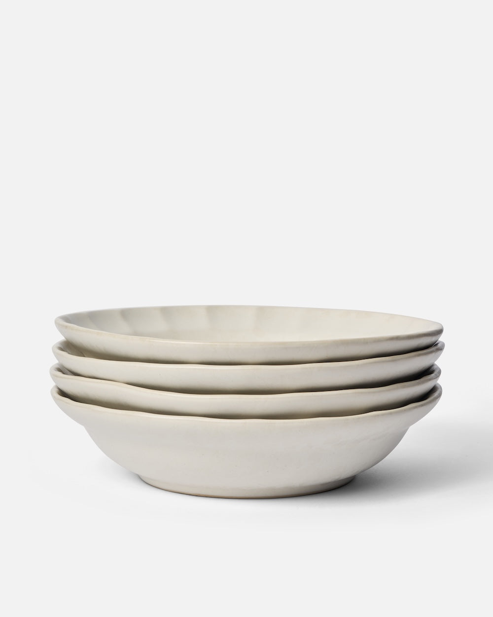 Stack of four white ceramic pasta bowls with textured rims on a white background