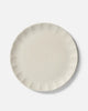 Cream-colored ceramic dinner plate with scalloped edges, minimalist design by Marion Grasby
