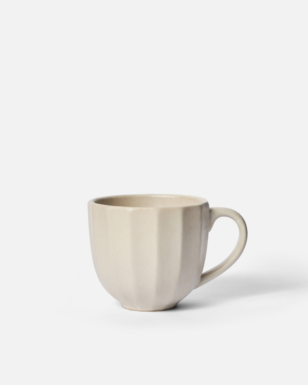 Cream ceramic mug with fluted design on white background, minimalist drinkware