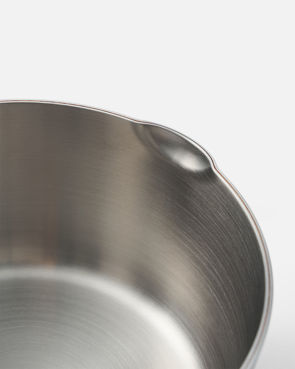 Close-up of a stainless steel cookware rim with a pouring spout on white background