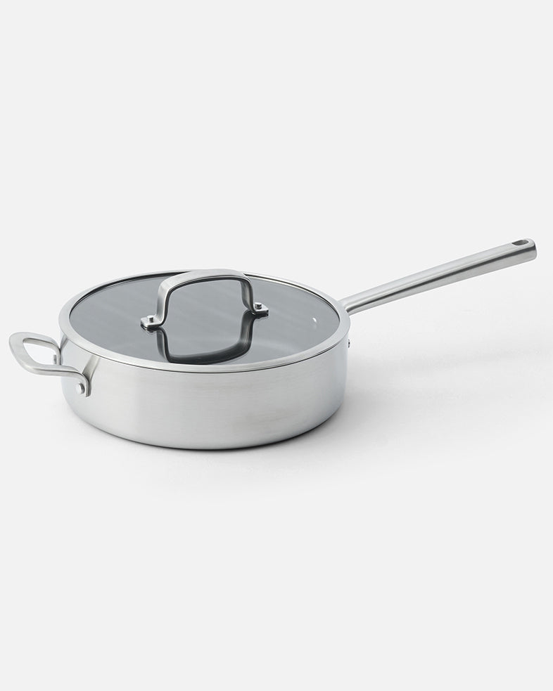 Stainless steel sauté pan with glass lid and long handle on white background