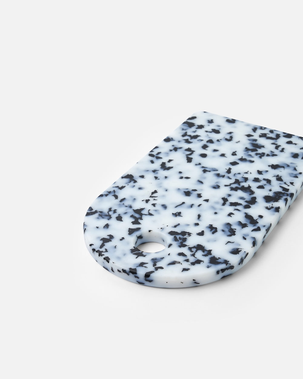 Speckled white and black resin cutting board with rounded edge and hanging hole on white background