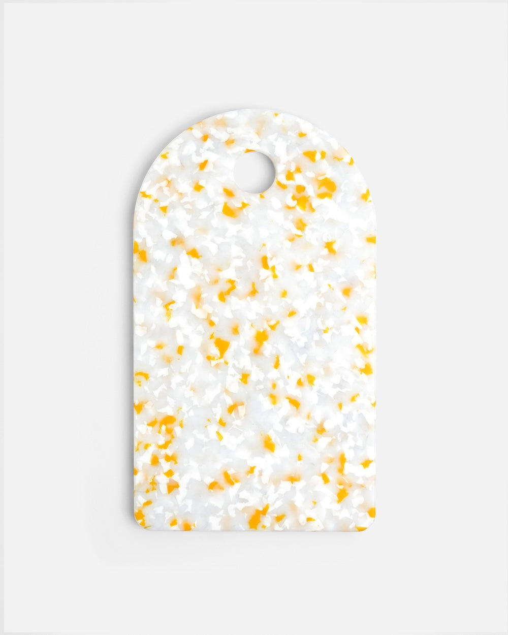 Rectangular white and yellow terrazzo cutting board with rounded top and handle hole