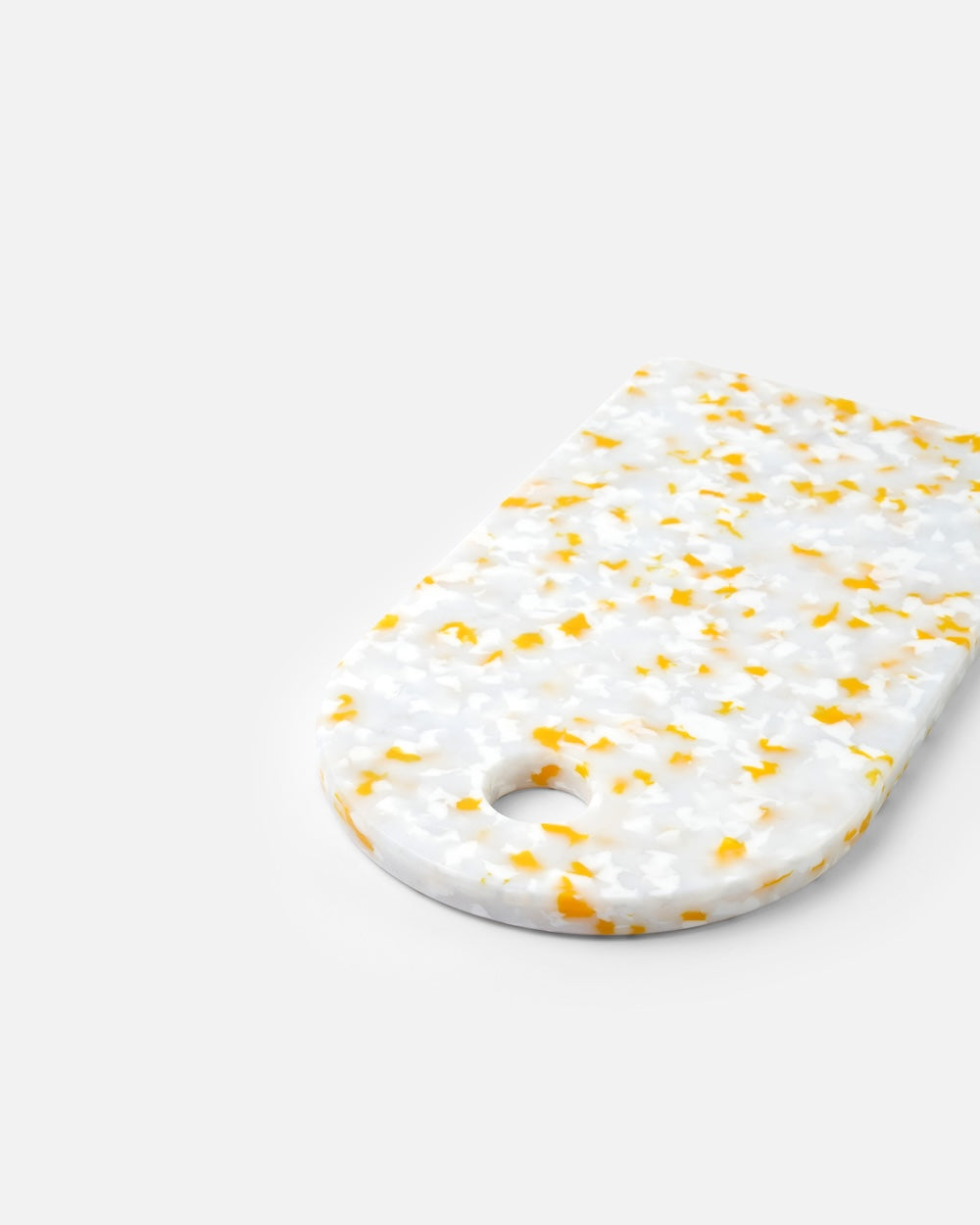 White terrazzo cutting board with yellow accents and rounded corner, on neutral background.