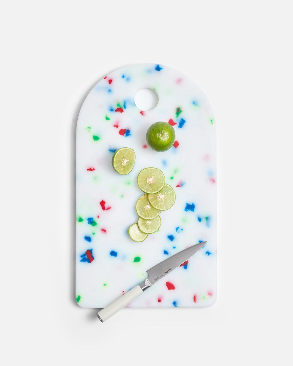 White cutting board with colorful confetti pattern, knife, and sliced lime on white background