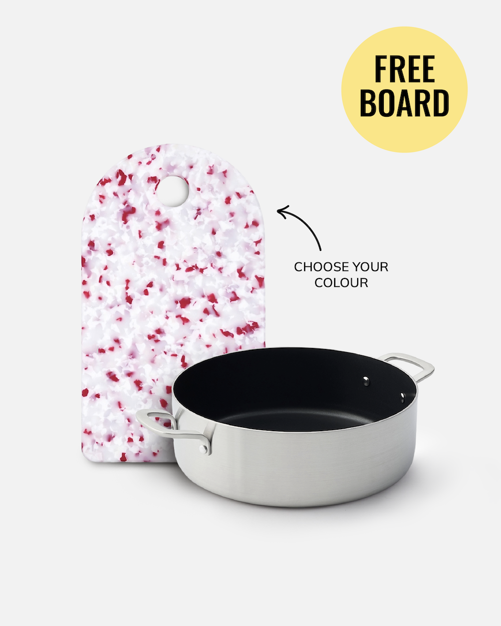 A stainless steel saucepan with a black interior is shown in front of a white cutting board with red speckles on a light gray background. A yellow circle reads 'FREE BOARD' with an arrow pointing to the cutting board and text reading 'CHOOSE YOUR COLOUR'.