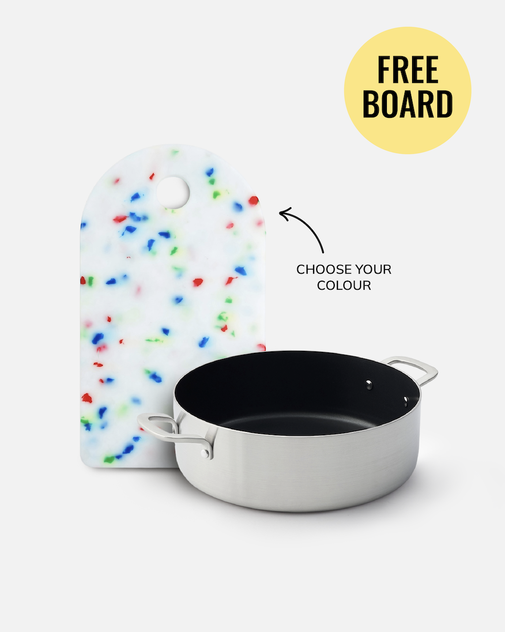 A stainless steel saucepan with a black interior is shown in front of a white cutting board with colorful speckles, on a light gray background. A yellow circle reads 'FREE BOARD' with an arrow pointing to the cutting board and text reading 'CHOOSE YOUR COLOUR'.