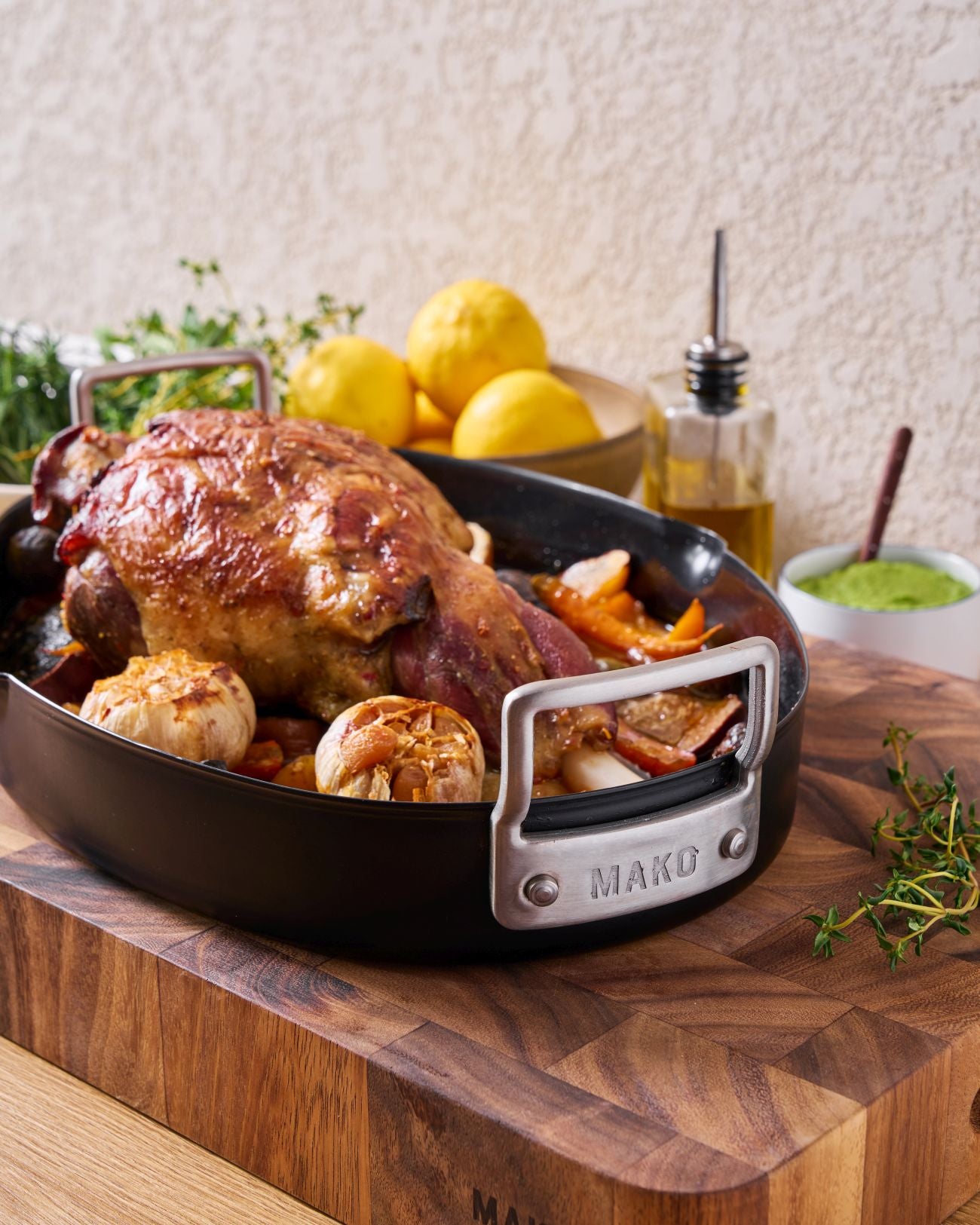 Slow-Roasted Leg of Lamb with Herb Yoghurt Marinade Recipe CookDineHost  finished lamb in pan on benchtop with lemons and oil in background