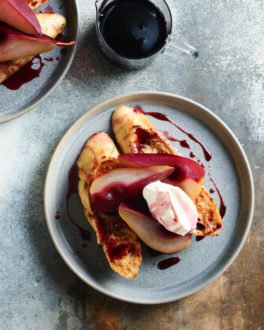 French toast topped with poached pears, whipped cream, and berry syrup on a ceramic plate