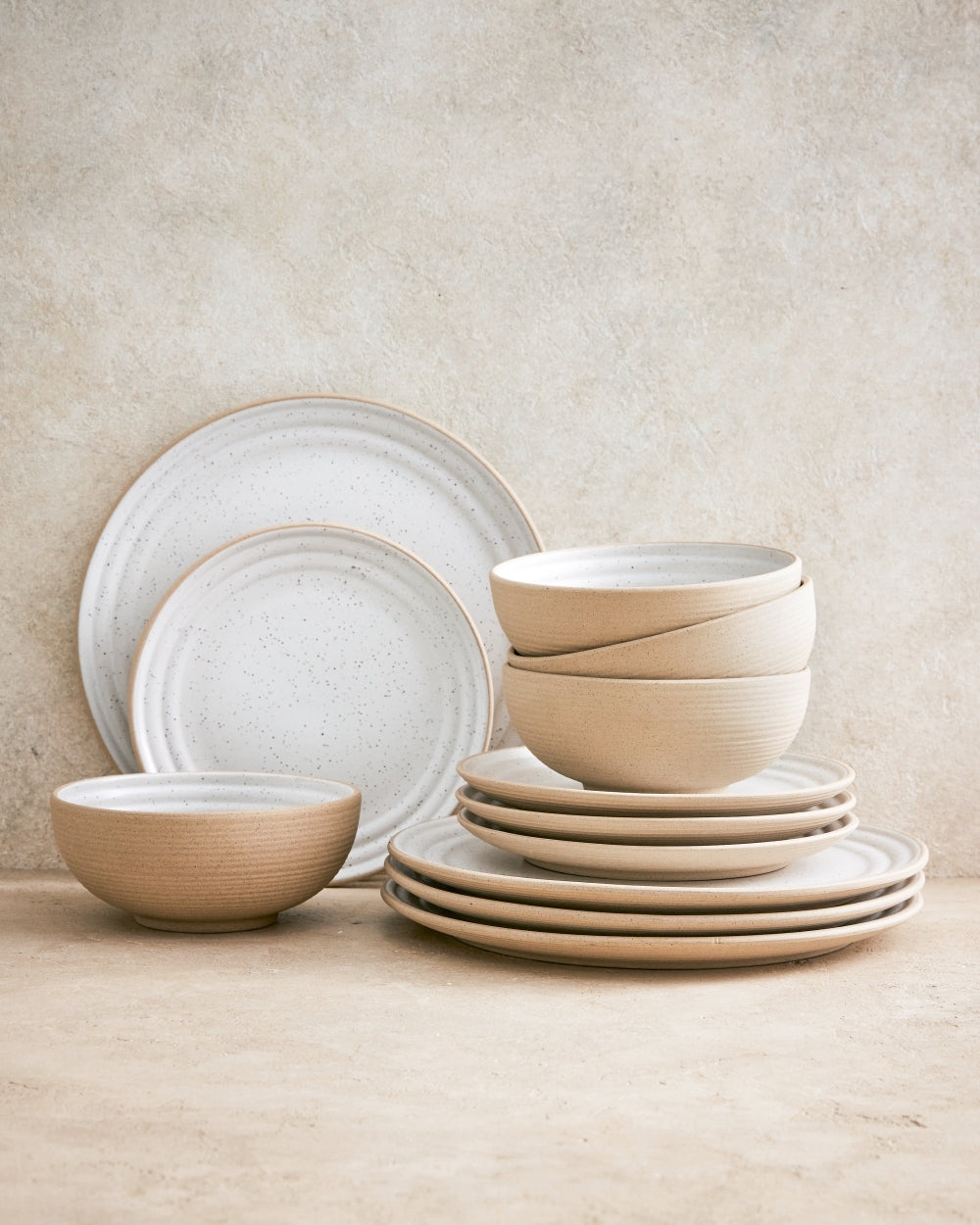 Set of four beige ceramic cereal bowls stacked with matching rustic plates on a neutral background.