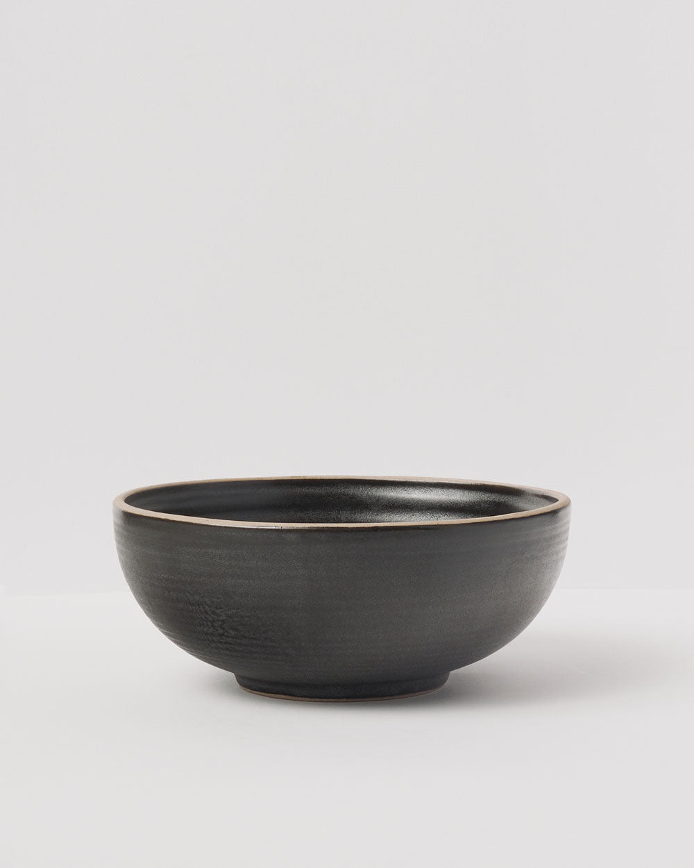 Anaya Charcoal Cereal Bowl Set features a handcrafted stoneware bowl with a deep charcoal finish and subtle glaze variations. The bowl has a rounded shape with smooth curved sides and a slightly raised rim against a light background, showcasing its modern minimalist design.