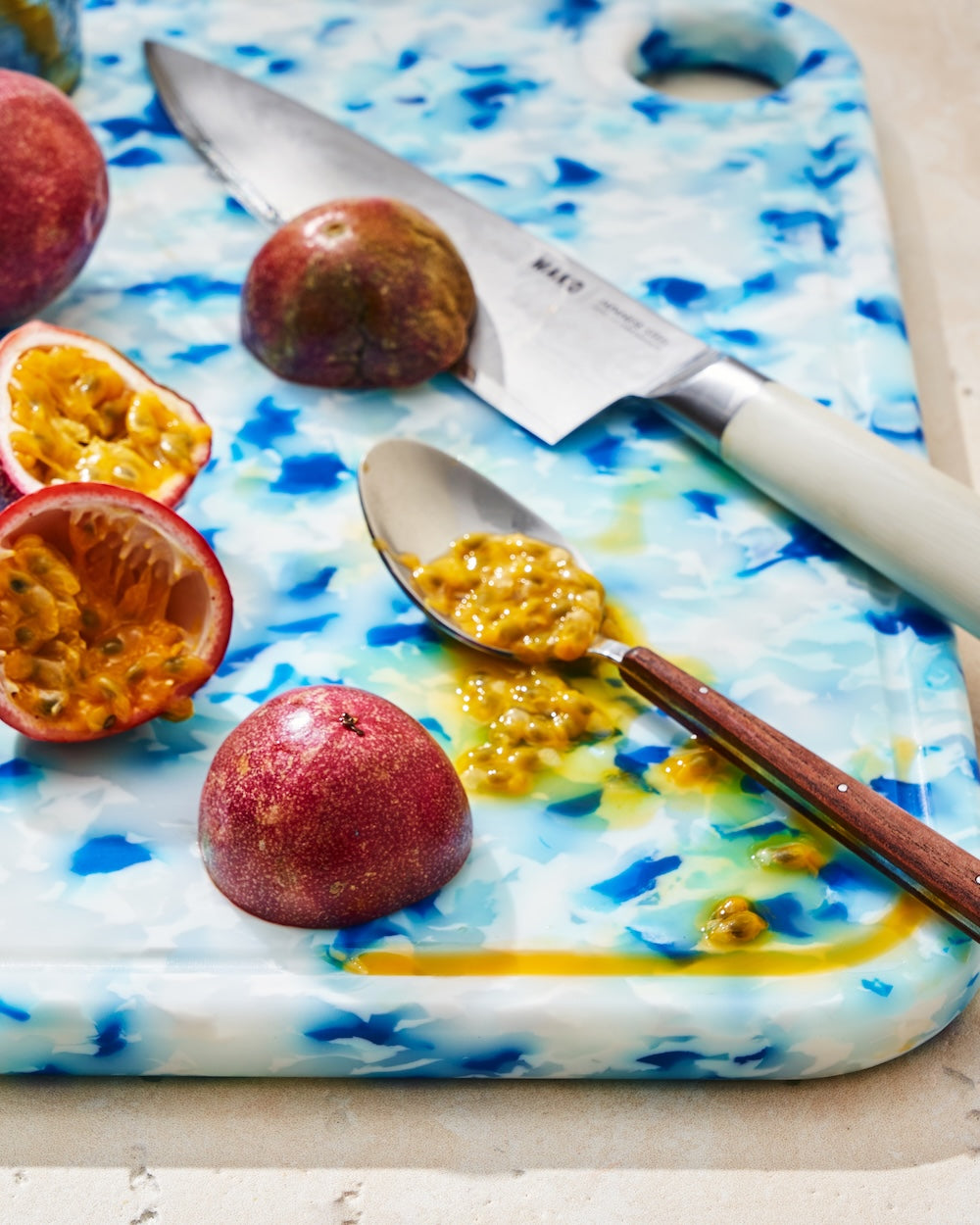 Blue recycled chopping board with passion fruit, spoon, and kitchen knife