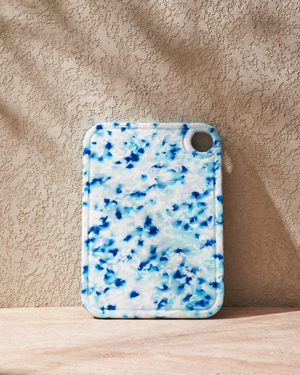 Asoke recycled chopping board by Marion Grasby in blue and white speckled design against textured beige wall