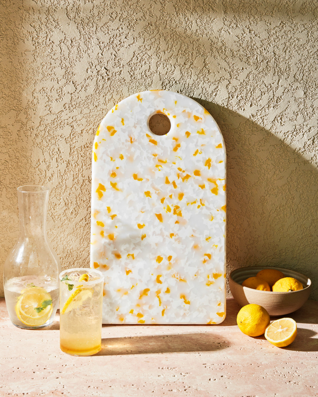 lemon-patterned recycled chopping board with glass pitcher, drink, and fresh lemons