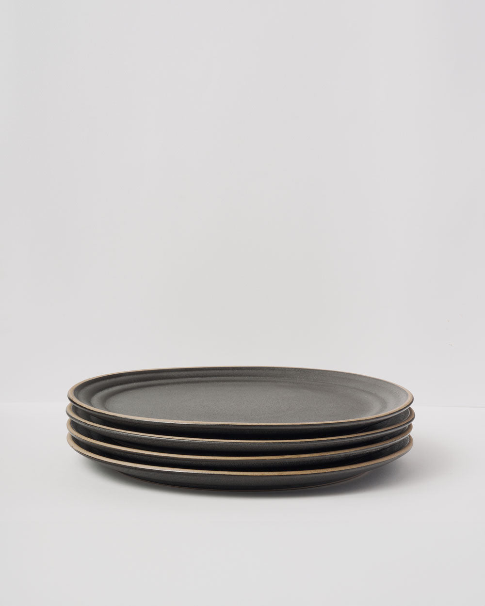 Anaya Charcoal Dinner Plate Set of 4 - Four stacked modern dinner plates in matte charcoal grey stoneware with subtle raised rims against white background, showcasing minimalist design and handcrafted quality