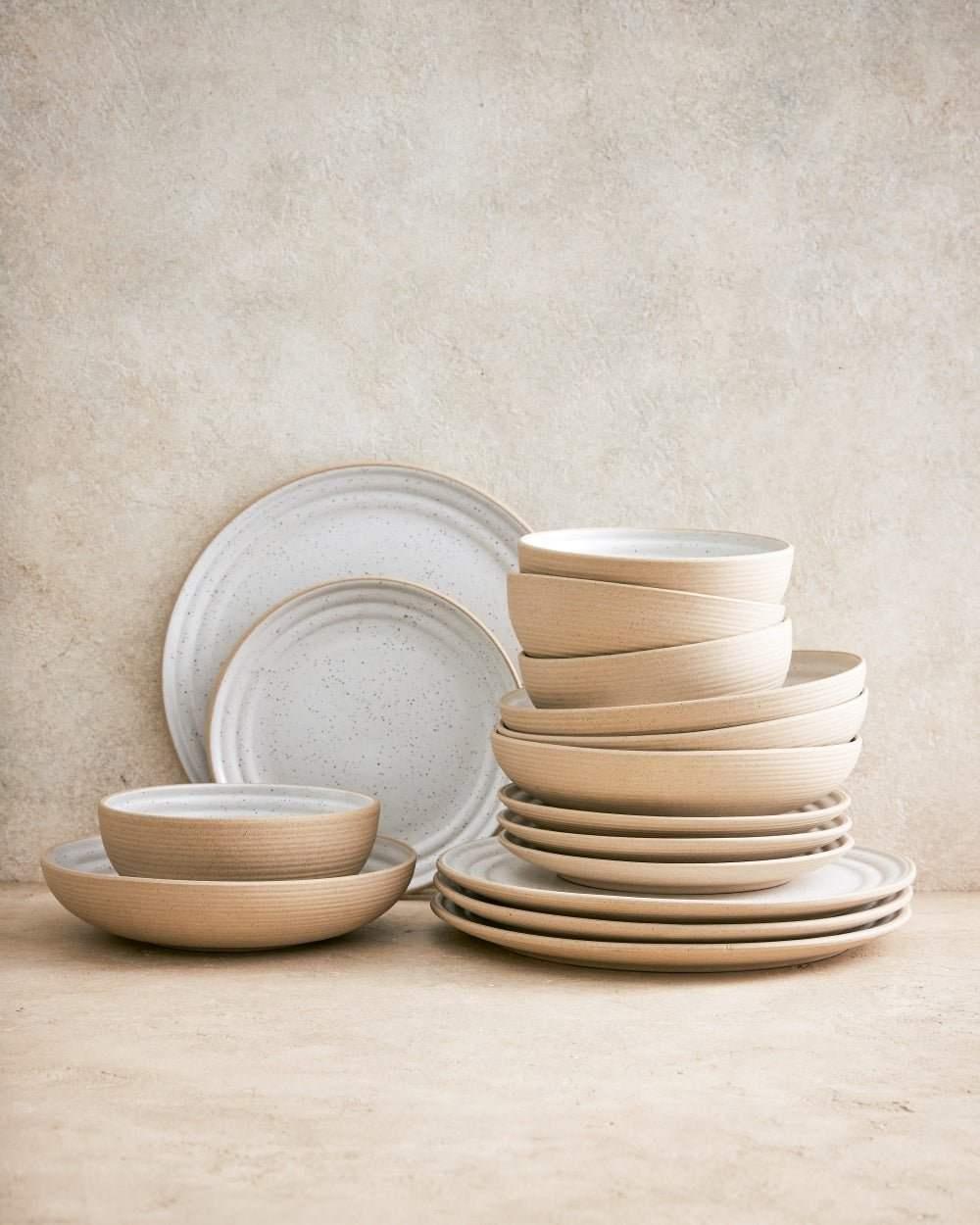 Stacked ceramic dinner plates and pasta bowls in beige and white with speckle detail