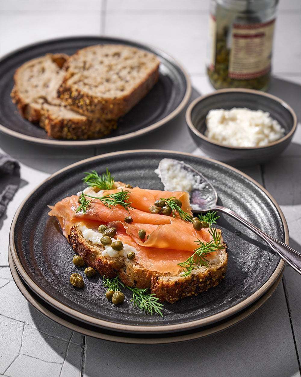 Asoke charcoal 24-piece dinnerware set with smoked salmon on multigrain bread, cream cheese, capers, and dill