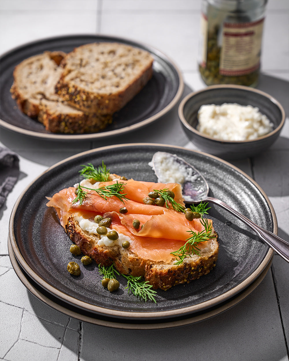 Charcoal ceramic dinnerware set with smoked salmon toast, capers, dill, side of bread and cream