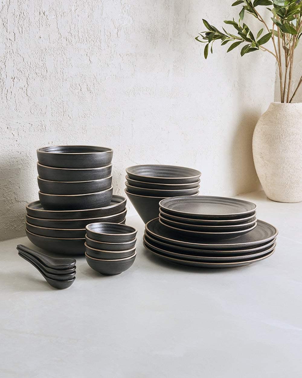 Charcoal ceramic dinnerware set with plates, bowls, and spoons on a light table.
