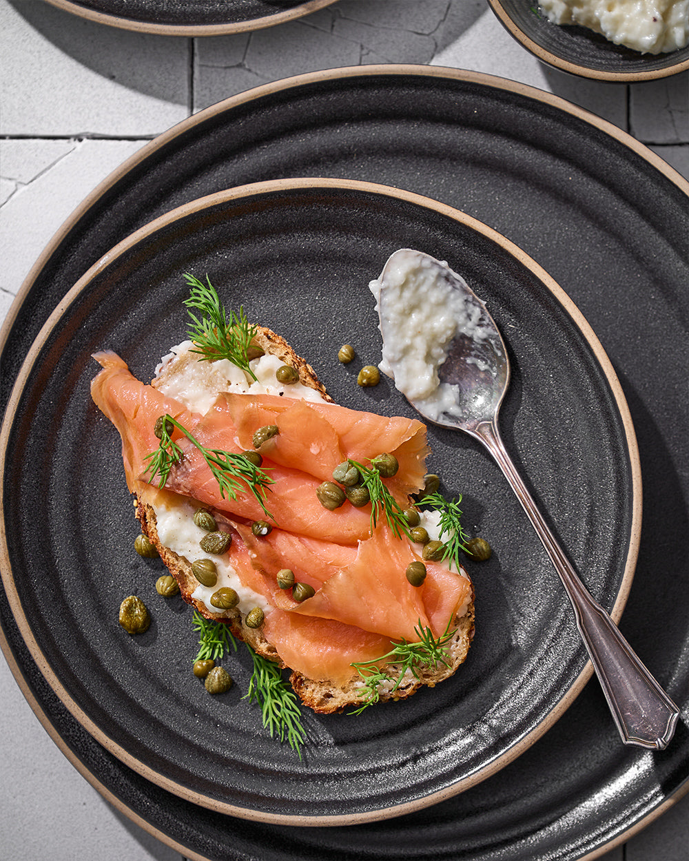 Charcoal ceramic dinnerware set with smoked salmon toast, capers, and dill garnish