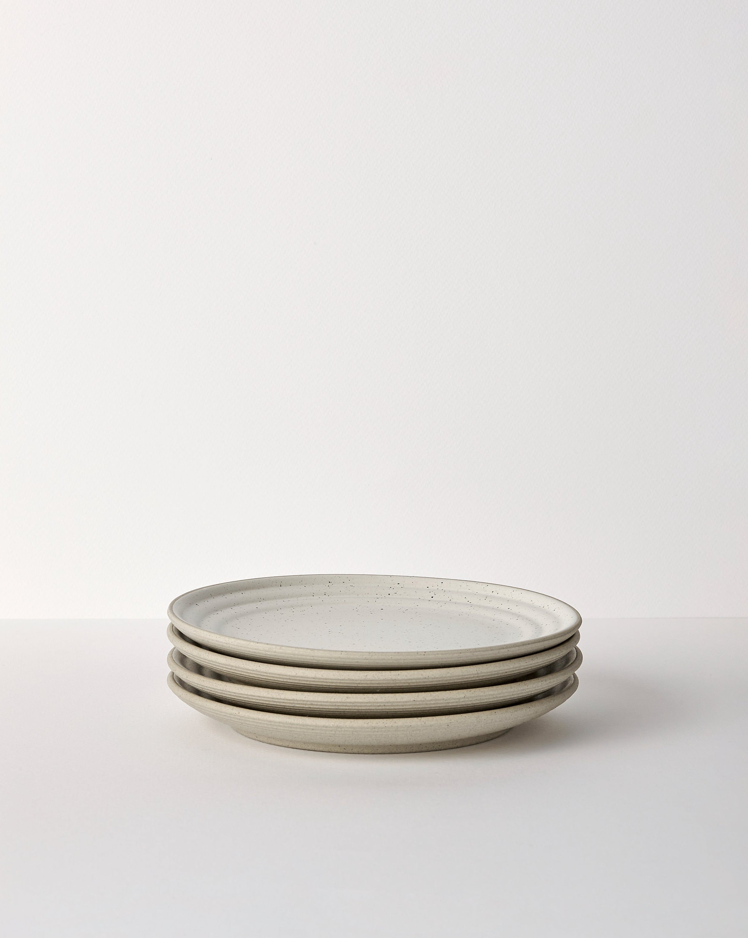 Stack of four speckled ceramic dinner plates in neutral tones on a white background