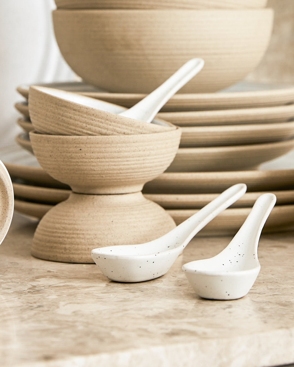 Neutral-toned stacked mini bowls with two white ceramic spoons on a marble surface