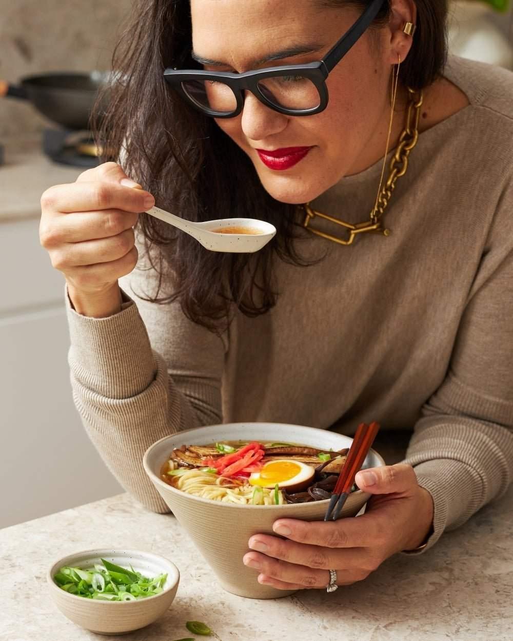 Woman enjoying ramen noodles with egg and vegetables in ceramic noodle bowl set