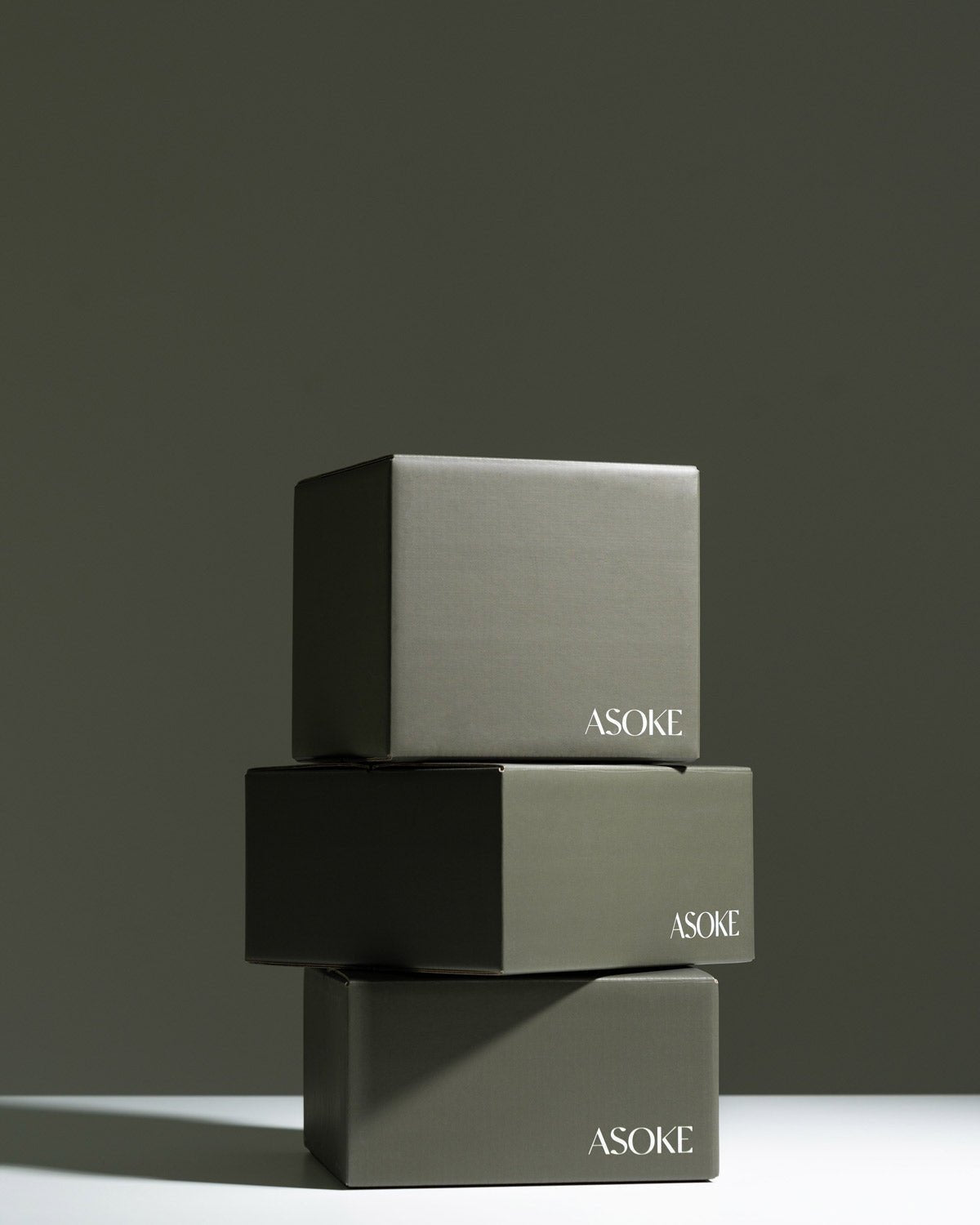 Stack of three matte gray ASOKE gift boxes with minimalist design on neutral background