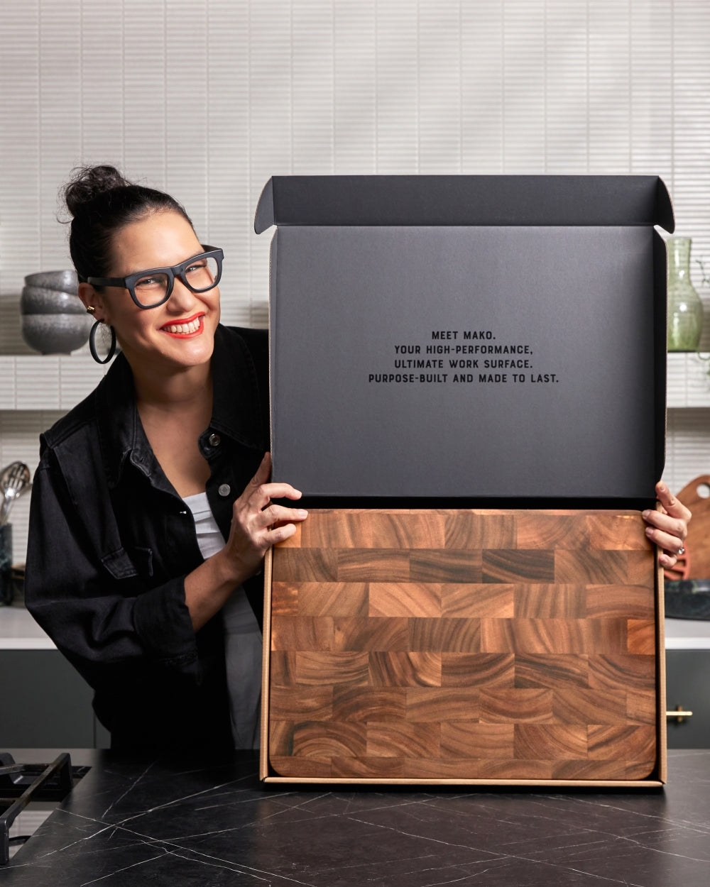 Person presenting a large wooden butcher block chopping board in a modern kitchen.