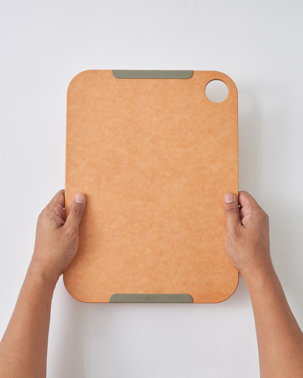 Hands holding a large non-slip wood fibre chopping board with rounded corners and a hole.