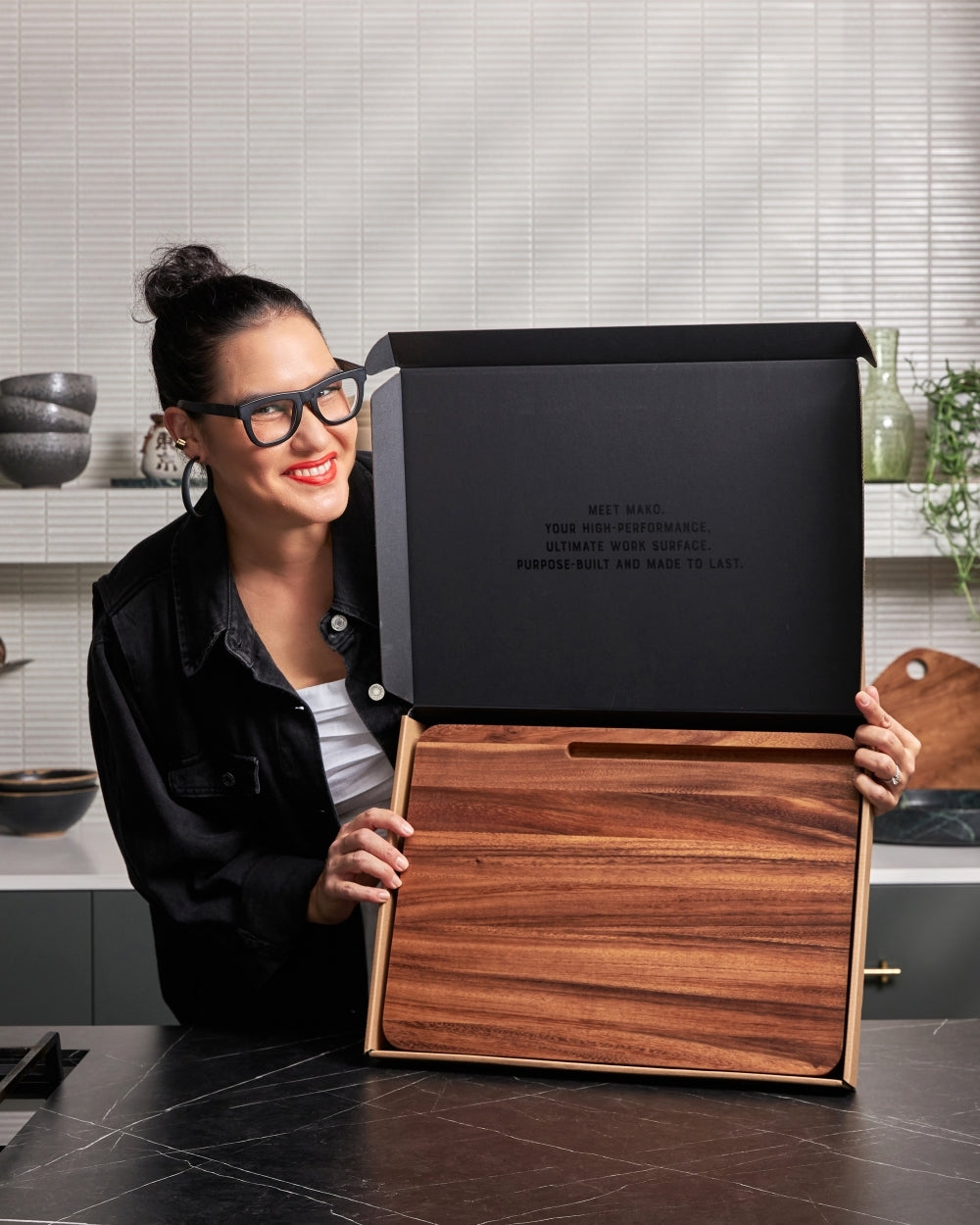 Woman presenting a wooden multi-use chopping board in sleek packaging on a kitchen counter