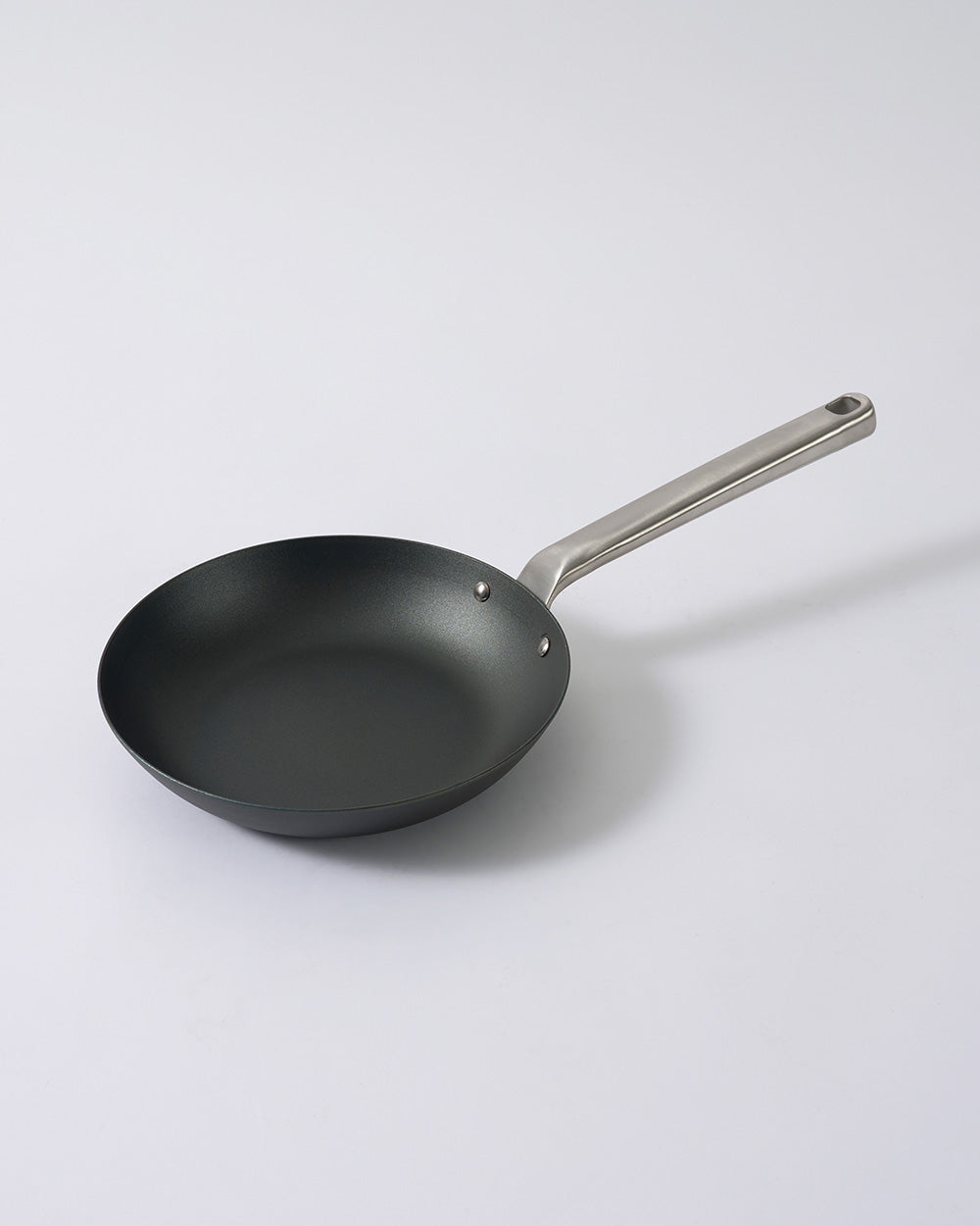 Black steel frying pan with stainless steel handle on a plain white background